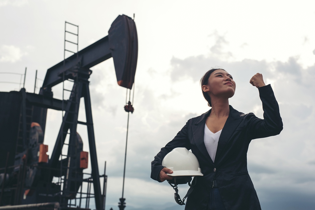 female-engineer-standing-with-working-oil-pumps-with-white-sky